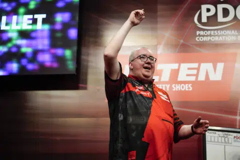 Ein Dartspieler, der seine Freude bei einem Wettkampf zeigt und den Arm in die Höhe hebt.